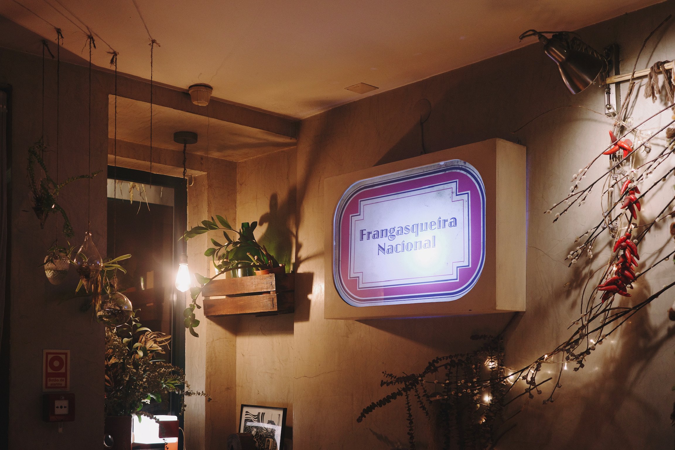 A light box that says Frangasqueira Nacional on a wall in a restaurant with plants and artwork as decorations.