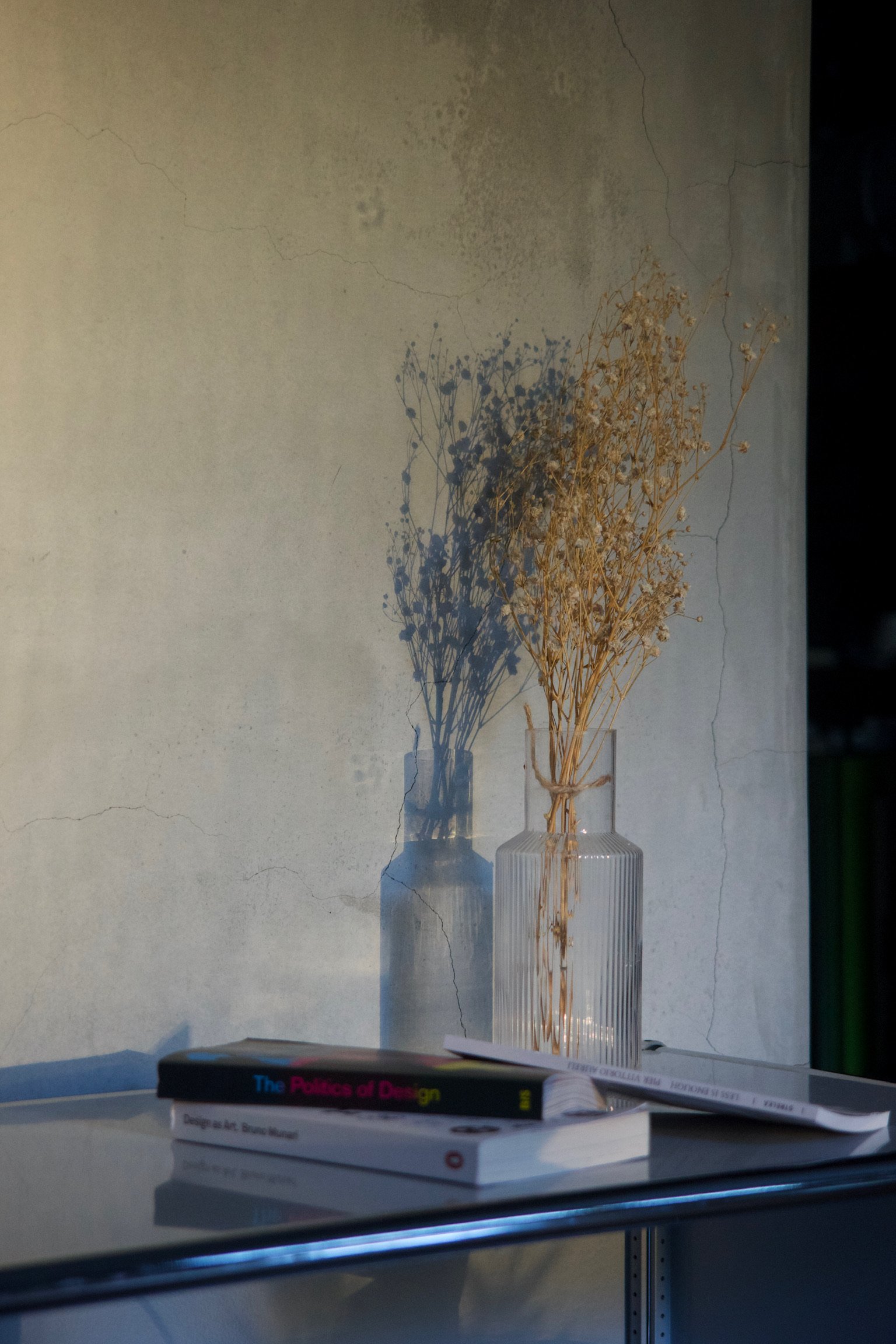 a glass vase with dried flowers on a white cabinet along with 3 books.