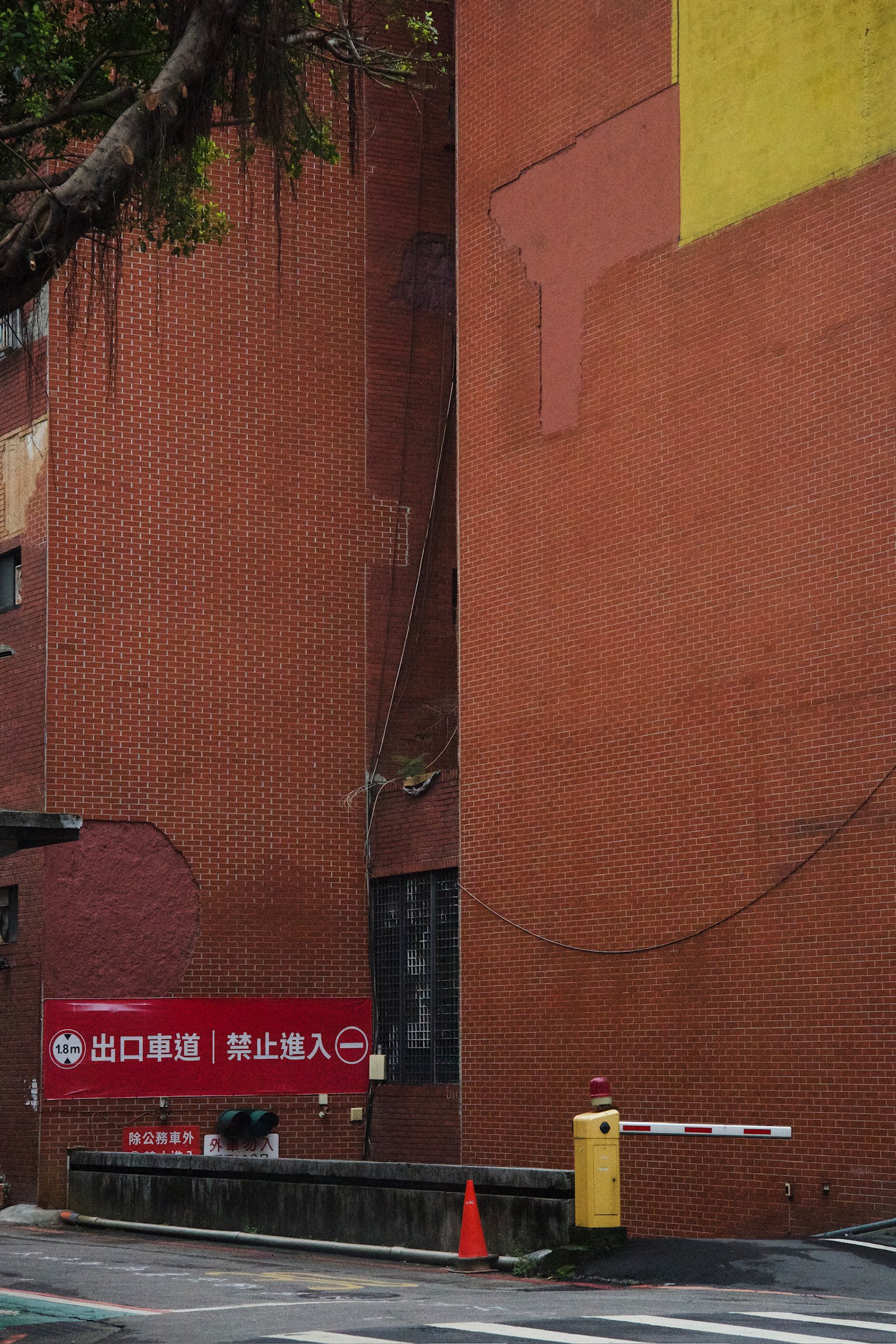 Tall Brick building with a yellow signpost to the parking lot underground and a yellow block of paint over the top right corner of the building.