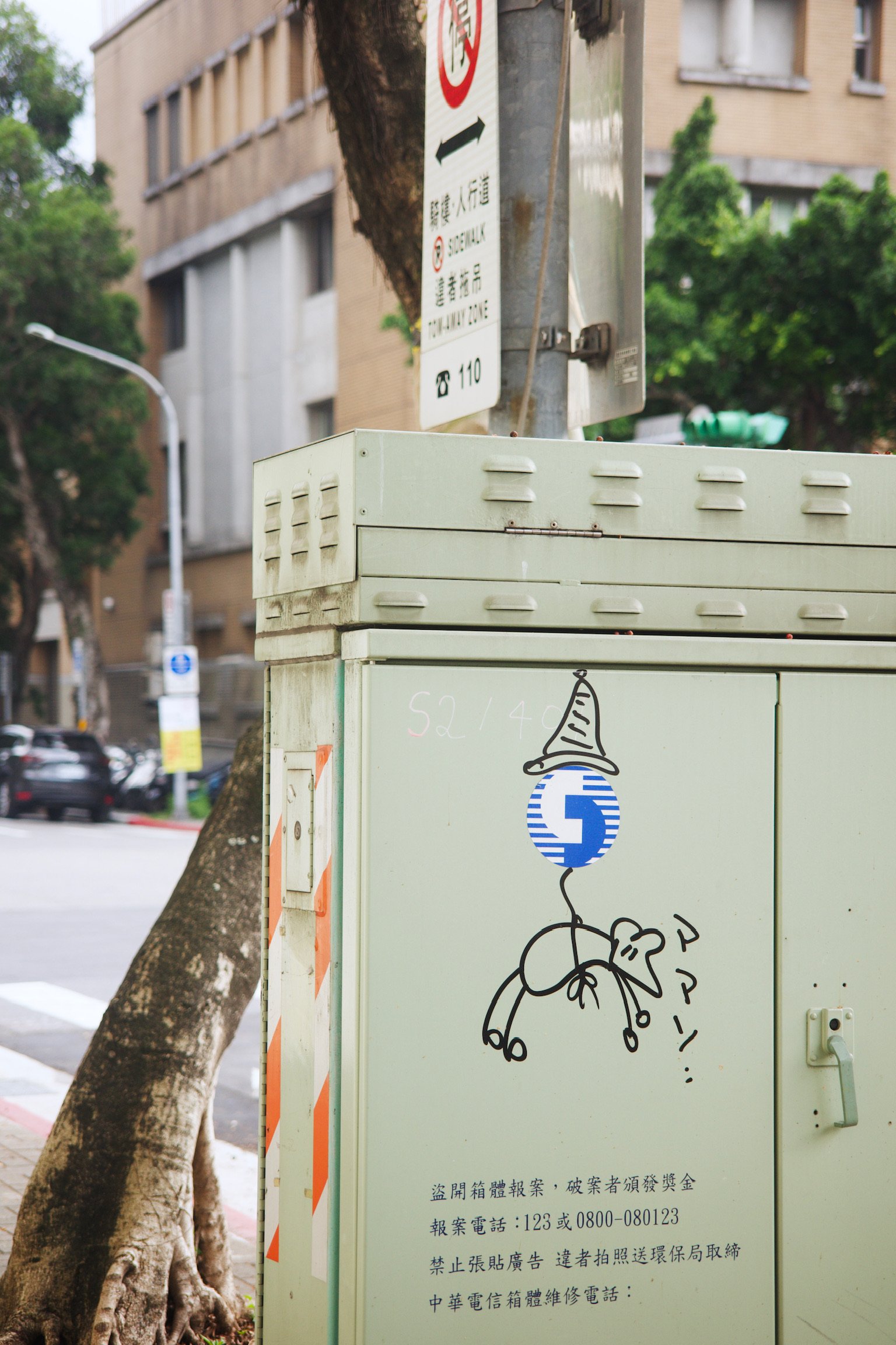 Graffiti on a electricity box with a mouse being hang by a thread across its body, saying ママン.