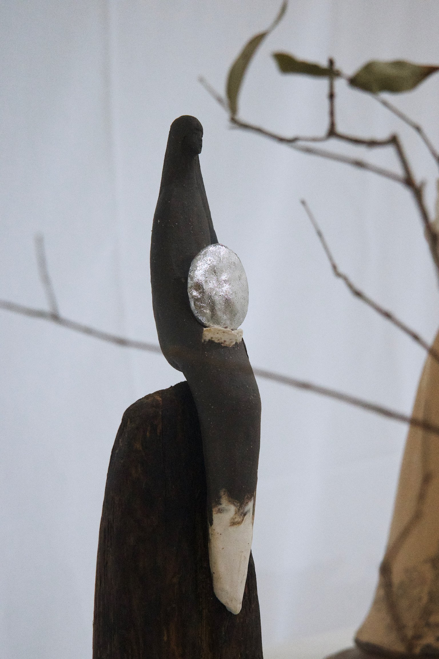 Sculpture of a slender woman holding a silver disc sitting atop of a wooden block.
