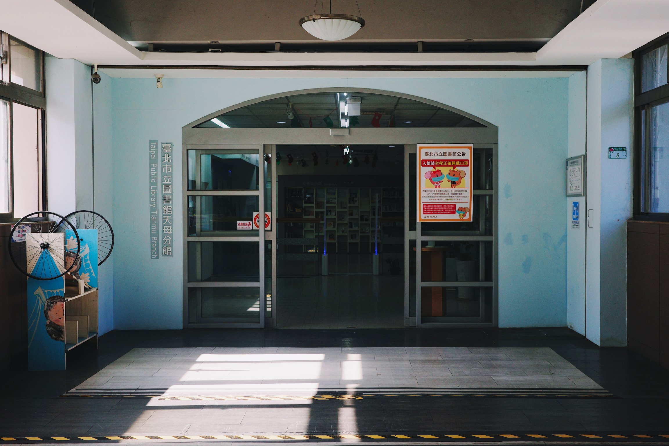 Entrance to a library with light blue walls and windows on both side and shadow on the floor.
