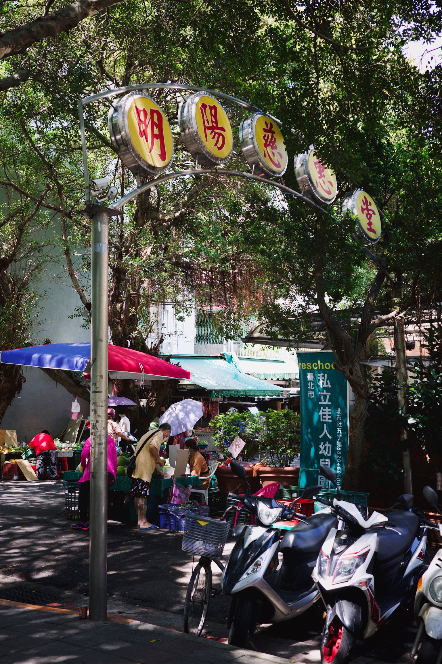 Sunny day. Entrance to a traditional market in Taipei, with street vendors, greeneries, and a arch named after a temple.