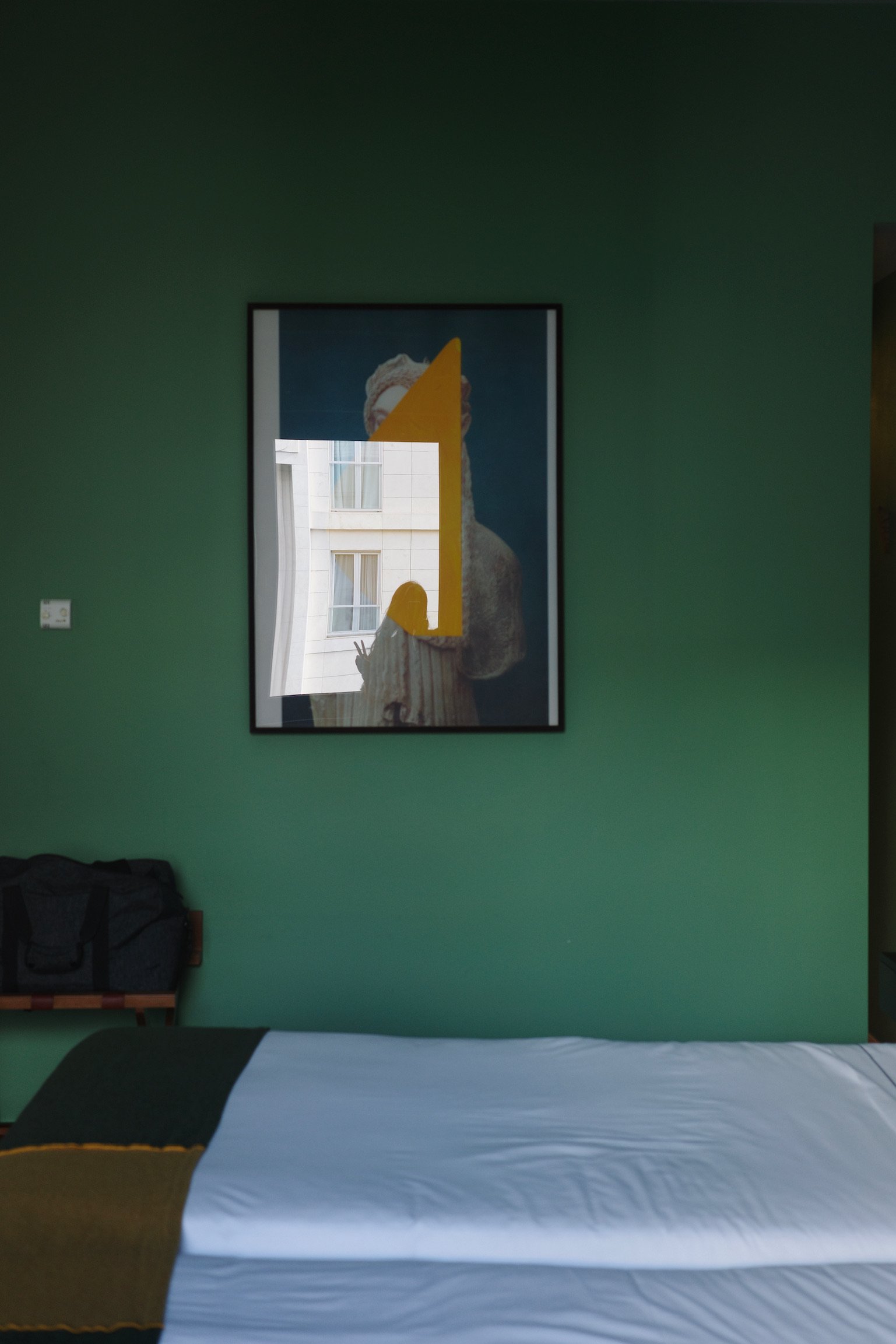 Selfie in the reflection of a framed painting in a hotel room with green walls and green throws.