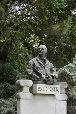 a statue of a one Bruckner in a park with a black bird perching on its hand