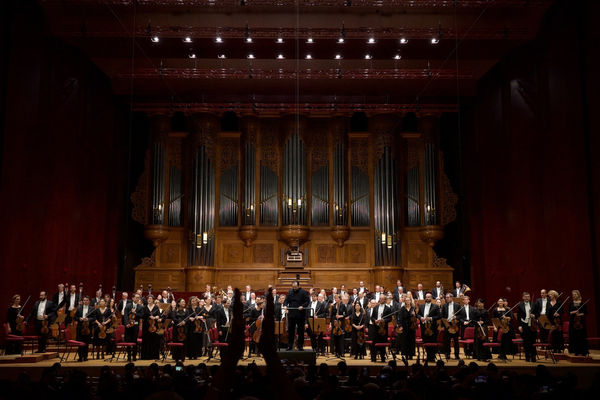 An orchestra and conductor at the center of the stage at the closing of a performance