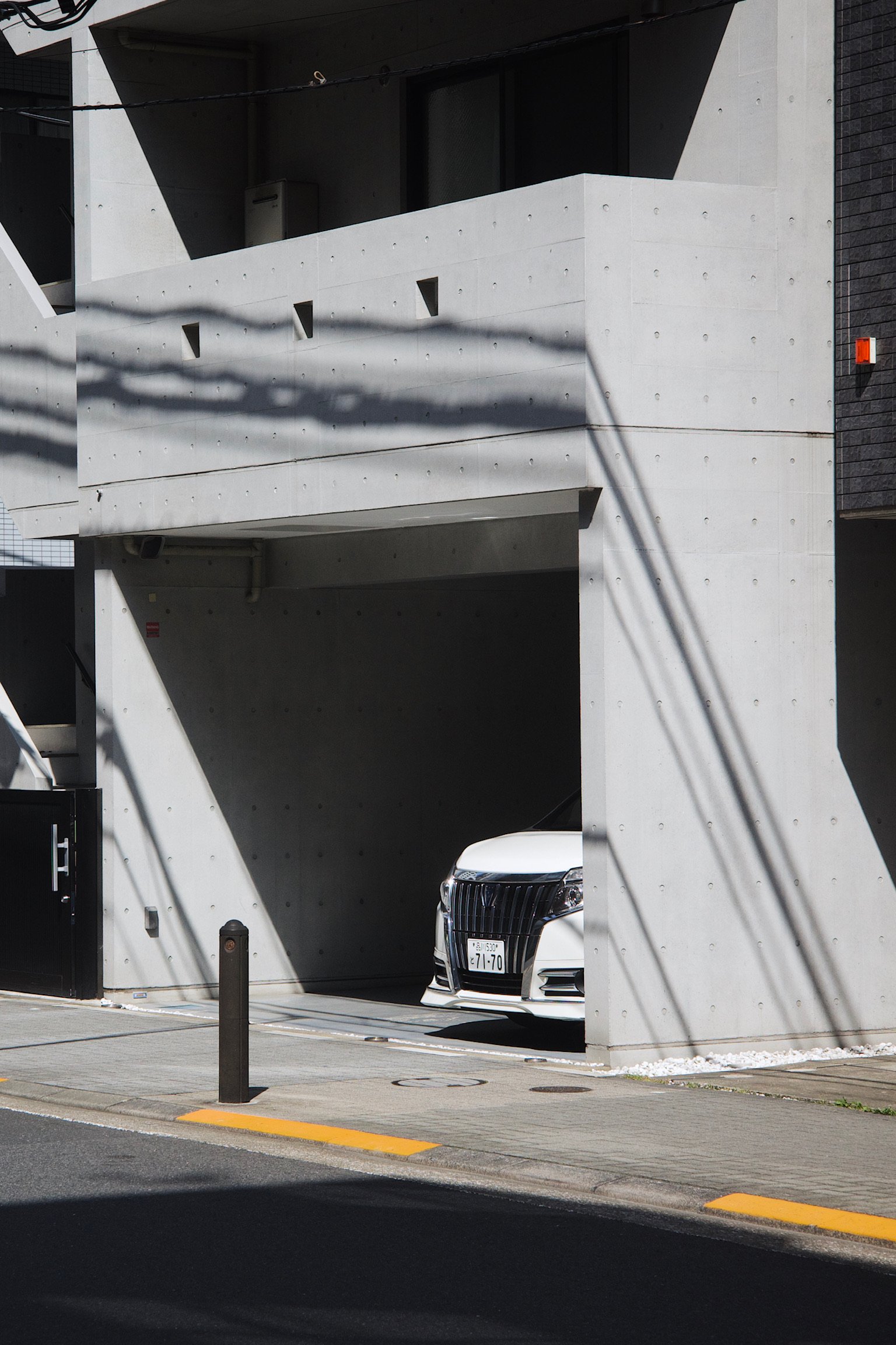 a car parked in a garage on the street level, white building with shadow of street lamps casted on the walls.