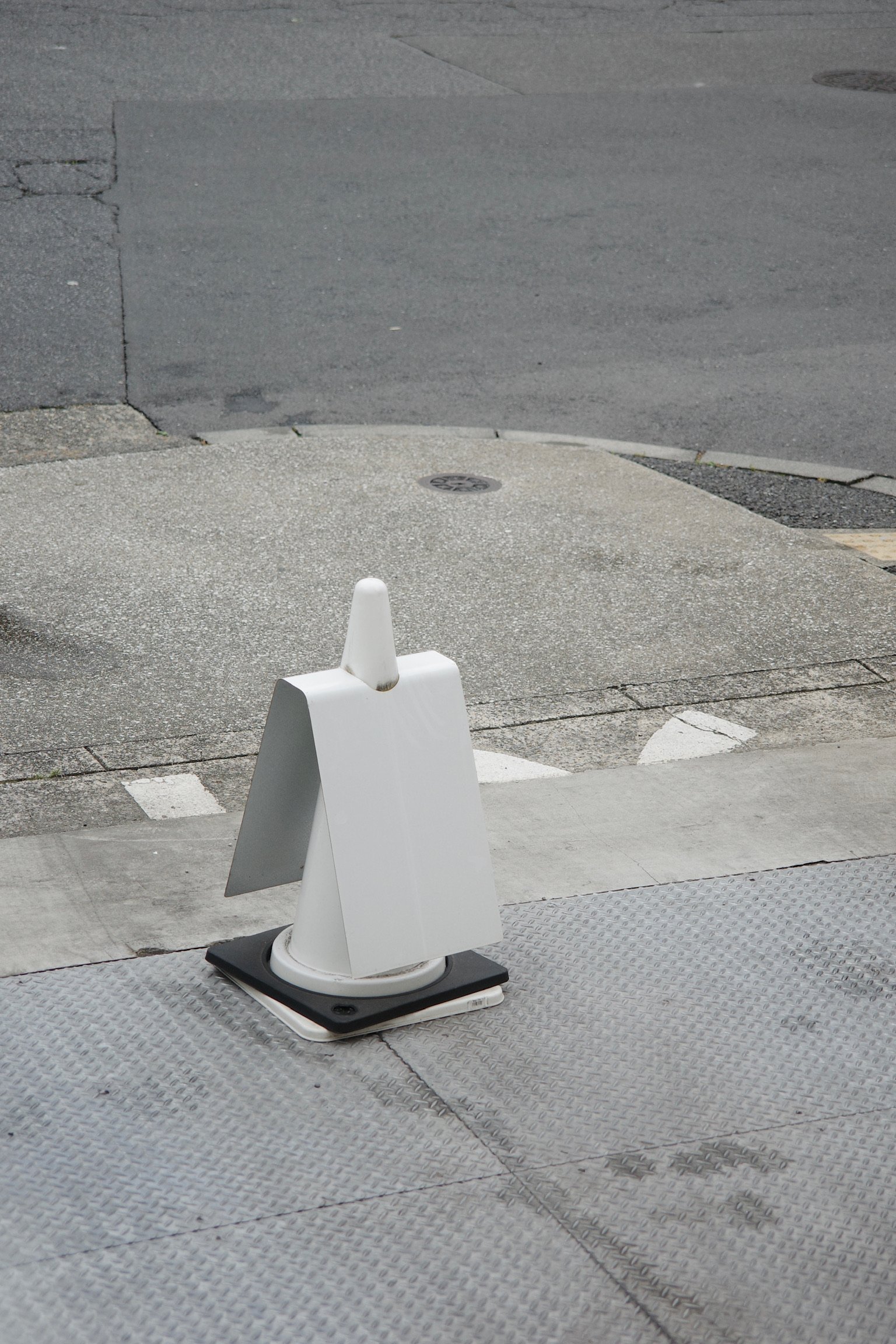 a white traffic cone with a white cardboard attached to it on a sidewalk.