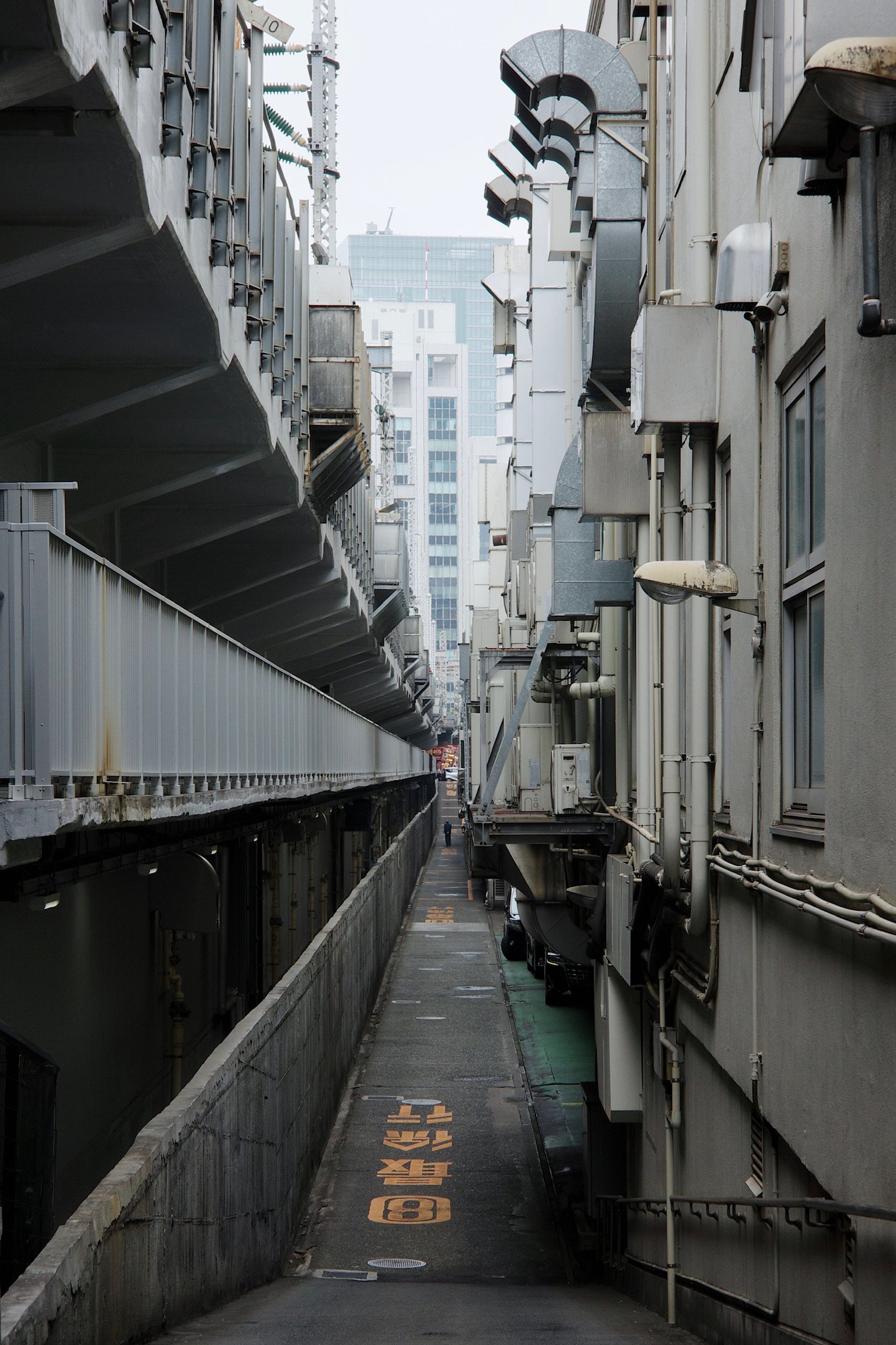 a narrow alleyway between buildings and a highway/overground.