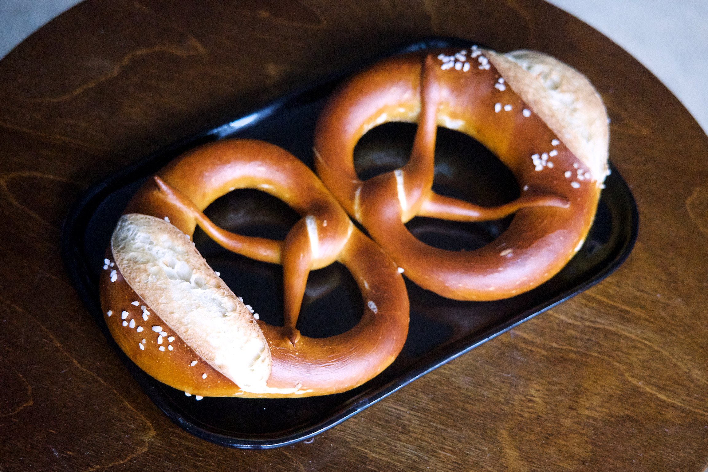 Two pretzels on a black rectangular plate facing each other.