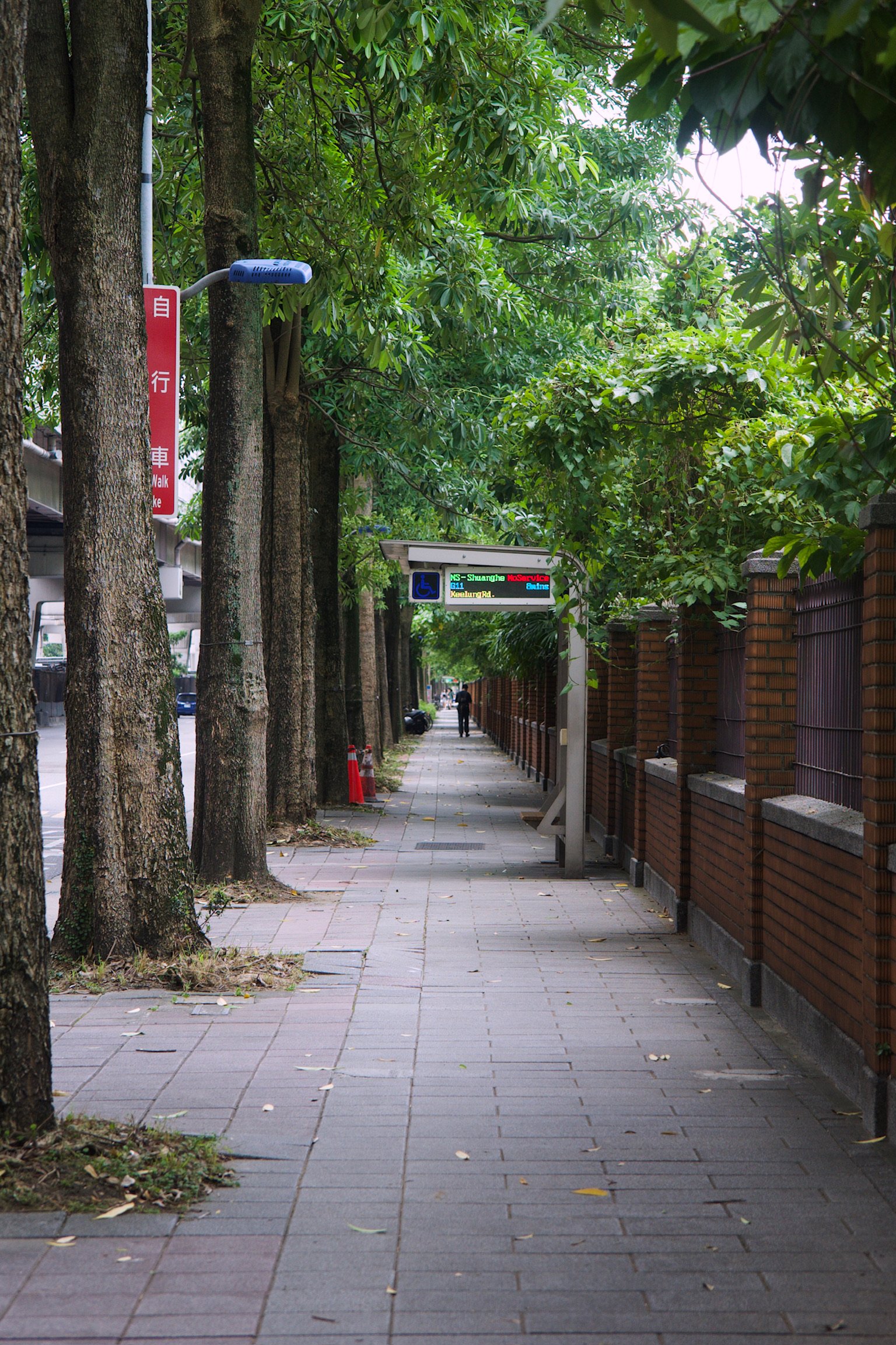 A sidewalk with trees and a bus stop.