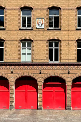 Brick building with arched windows and archways with bright red doors and the Berlin Fire Brigade logo.