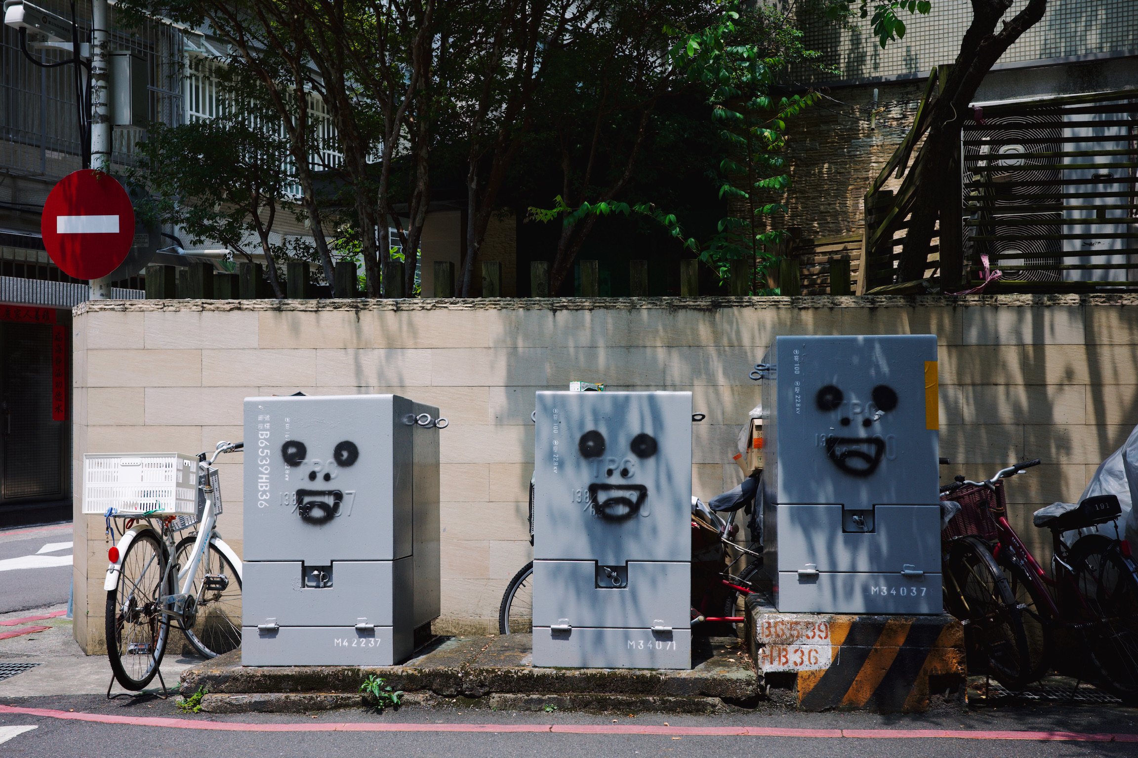 On a corner of a street there sat three gray transformer boxes with grimacing faces drawn on them.