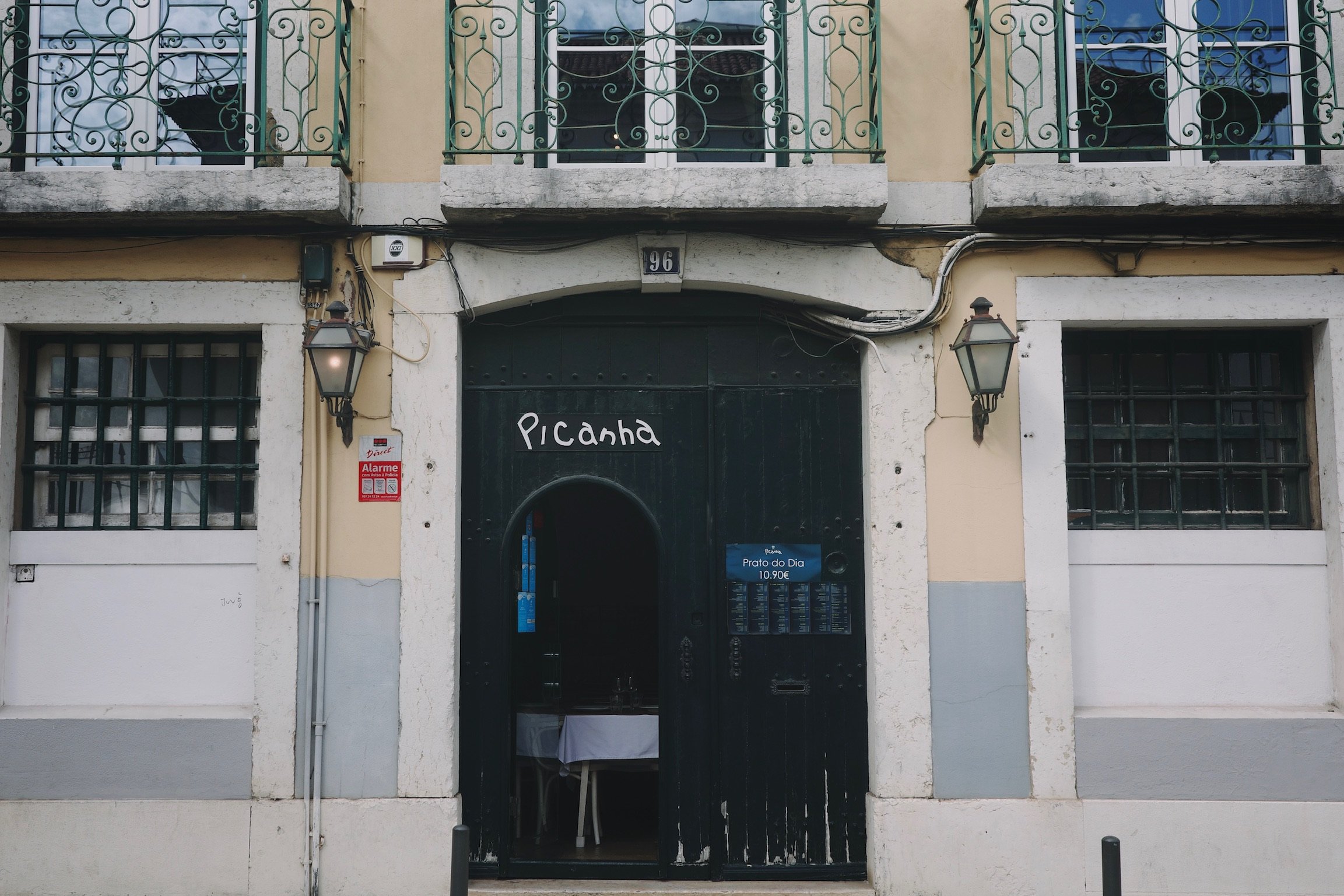 Shop from of Picanha a restaurant, featuring a dark green wide wooden door, with hand written sign. windows on the first floor featuring dark green rails.