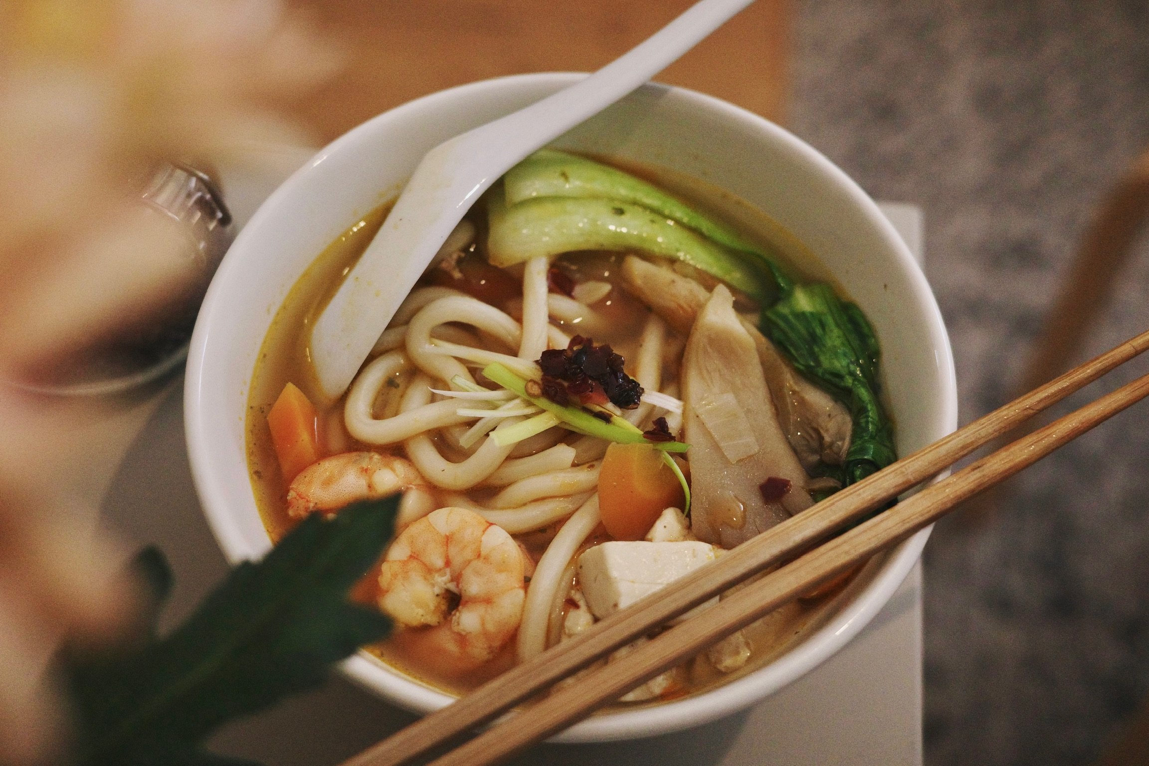A bowl of soupy udon noodles with bok choy, shrimp, tofu, carrot.