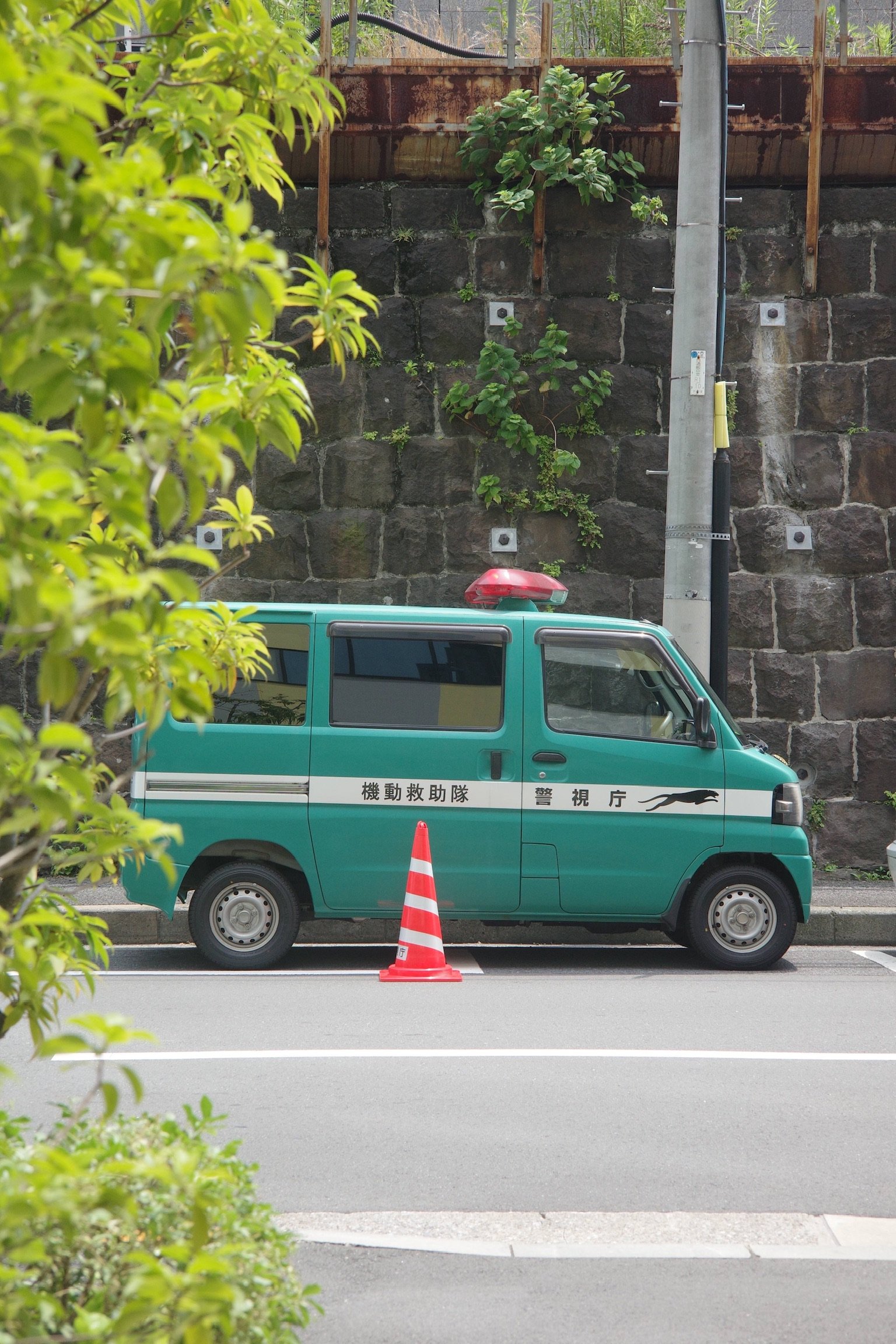 a green japanese police vehicle parked on the side of a road with traffic cones by it.