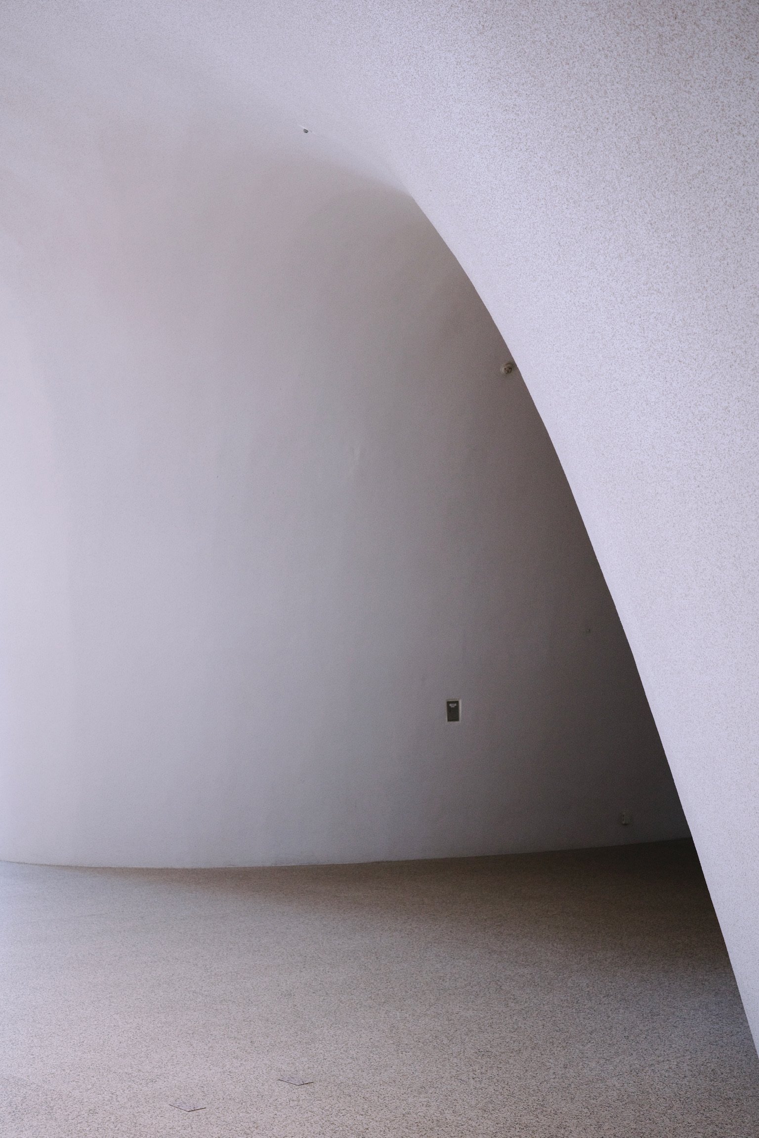 Interior space featuring smooth white walls, curved corners, and soft shadows.