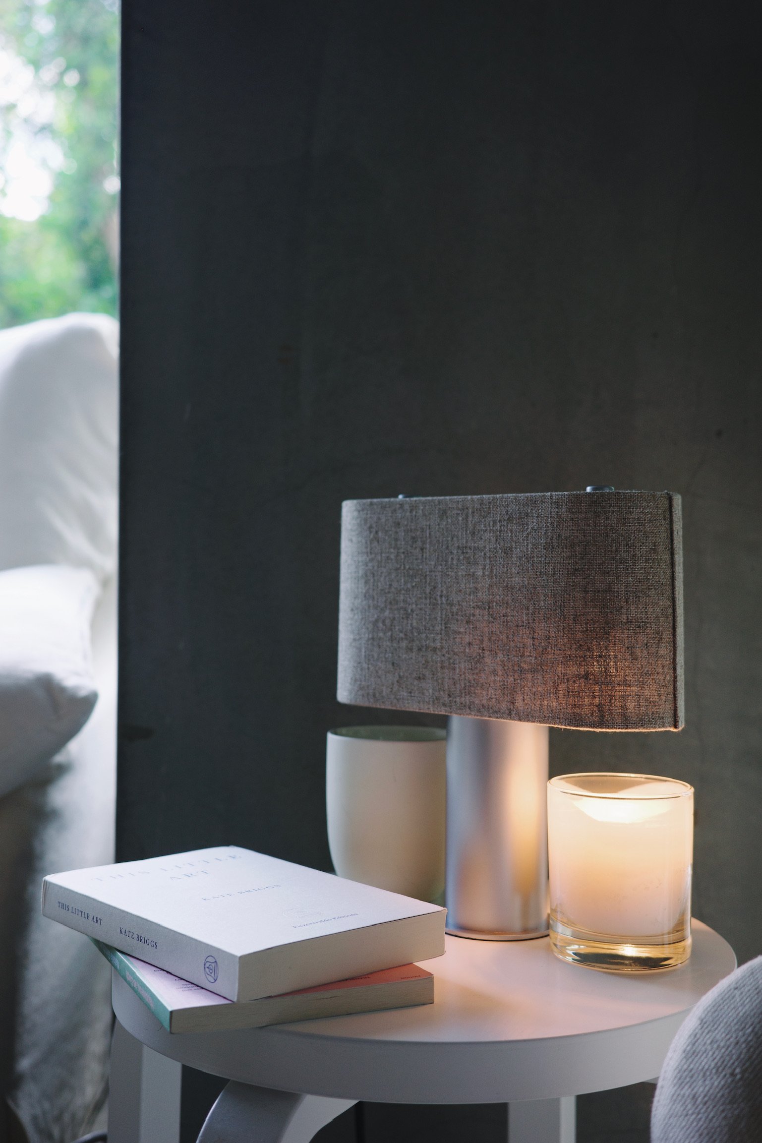 Duo candle warmer lamp by KIMU Design on a stool by two books against a concrete wall.