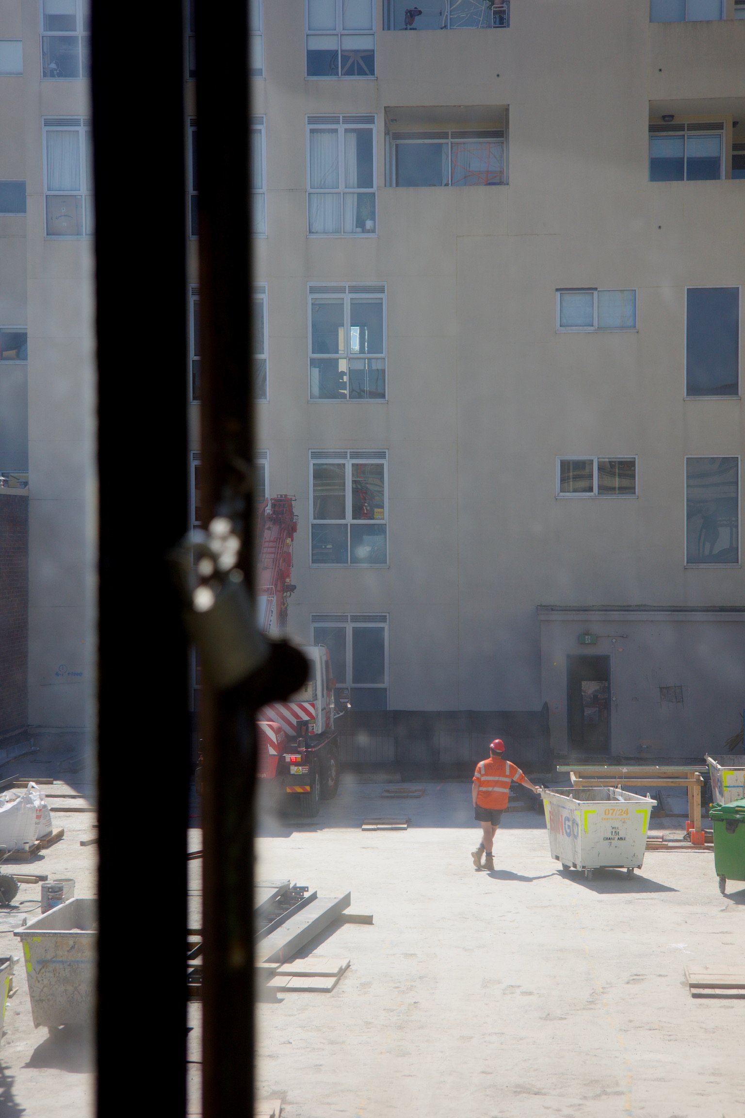 through a window, a person standing on a rooftop construction site wearing a bright orange vest