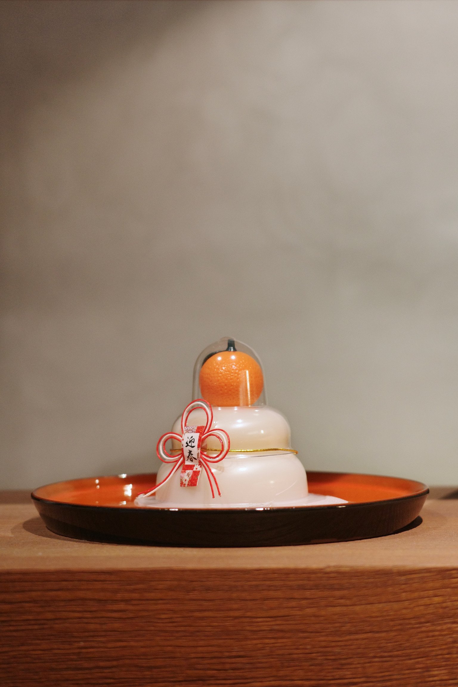 Kagami Mochi on a black and orange plate on a wooden shelf.