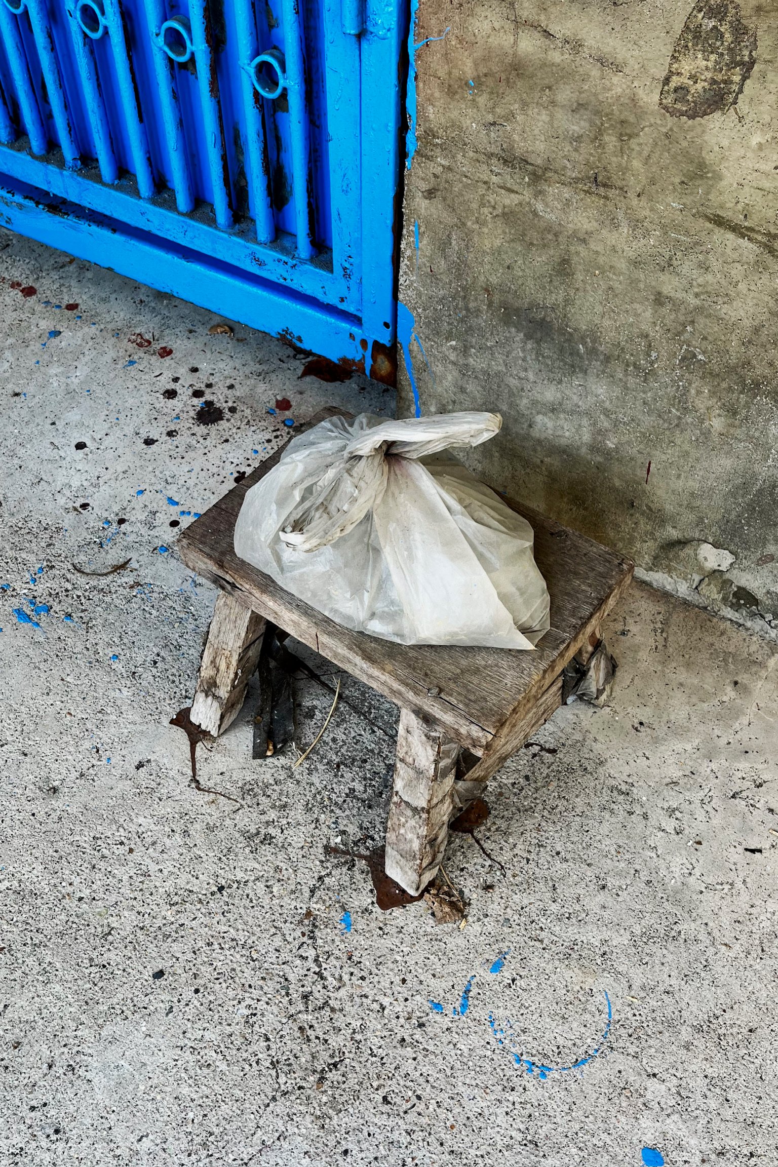 a plastic bag on a small stool by a steel bright blue door.