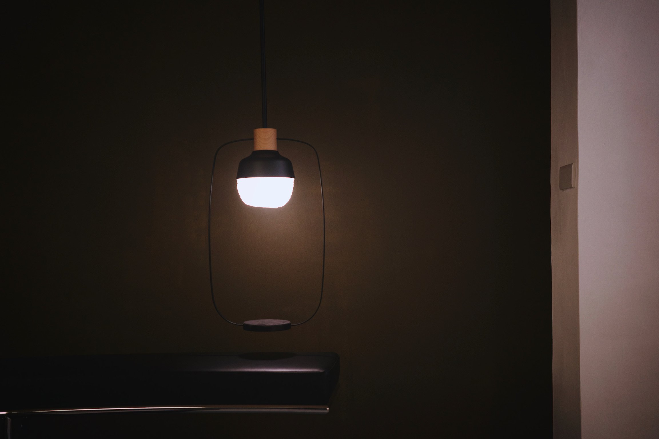 A lamp designed by KIMU Design in a dimly lit room floating above a leather couch.